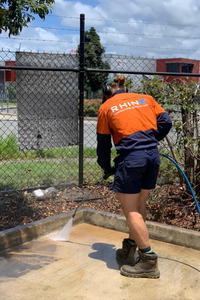 Personnel performing a deep clean service using a high pressure water hose to clean cement surface on a sunny day.