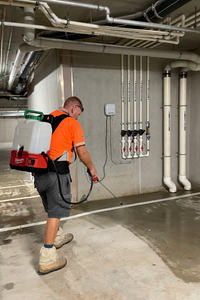 Rhino worker using a sprayer to clean a concrete floor in an underground space.