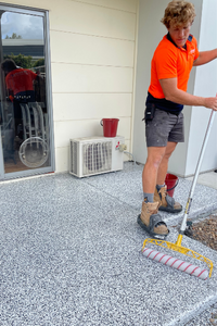 Rhino worker applying a coating to a concrete floor outdoors with a roller.