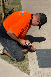 Rhino worker kneeling and working on a sidewalk using a power tool.
