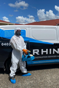 Rhino worker in protective gear with a disinfecting machine standing by a company van.