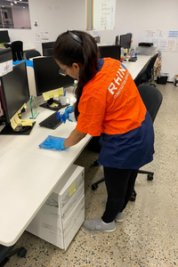 Rhino worker cleaning a desk in an office with computer workstations.
