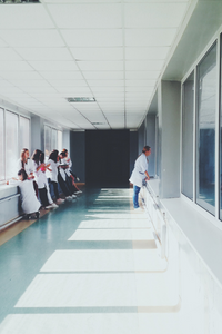 Group of people in white coats standing in a hallway with large windows.