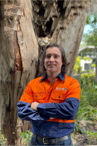 Rhino worker standing in front of a large tree with arms crossed.