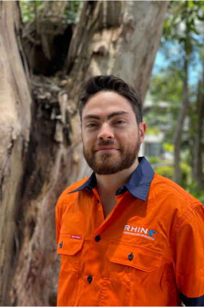 Rhino worker standing in front of a large tree wearing an orange Rhino shirt.